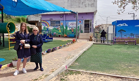 Kara Levy (left), co-founder of a nonprofit organization in Safed, and Maggie Stewart-Sweet in front of the children’s school and the FOI-donated bomb shelter (far right).